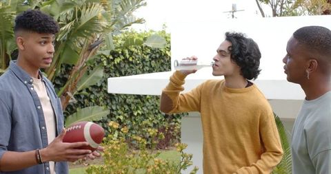 Diverse friends standing in backyard holding football and drinking from clear bottle