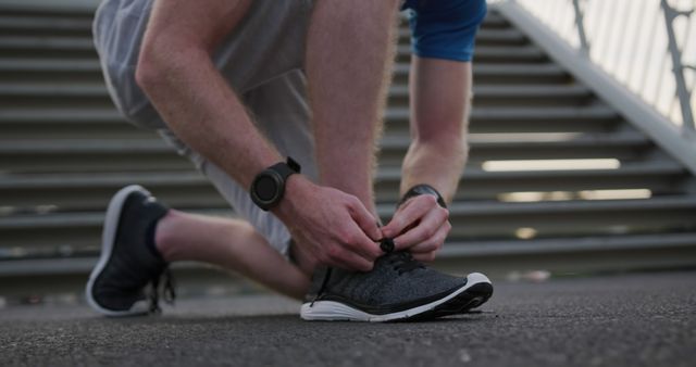 Lowsection of caucasian man tying his shoes by stairs in city. Sports, fitness, healthy living and outdoor activities, unaltered.