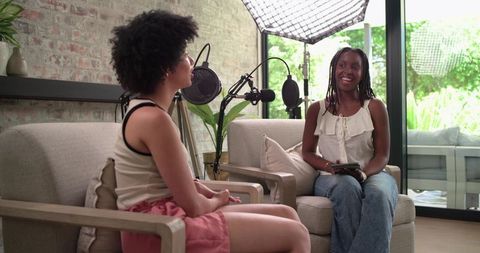 African american cohosts recording casual podcast in cozy living room studio with microphones