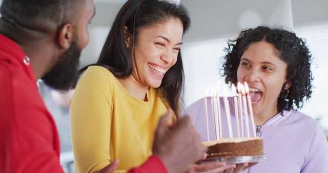 Happy moment captured of friends celebrating a birthday with a cake lit with candles. Image can be used for birthday celebration invitations, social media posts, blog articles on friendship, or promotional content for party supplies.