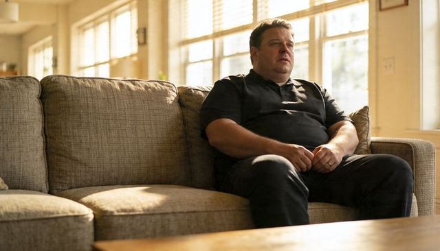 Contemplative man sitting on sunlit sofa wearing polo and clasping hands with wedding ring