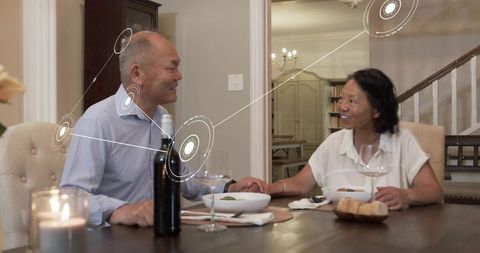 Chinese couple holding hands during candlelit dinner with digital connection graphics