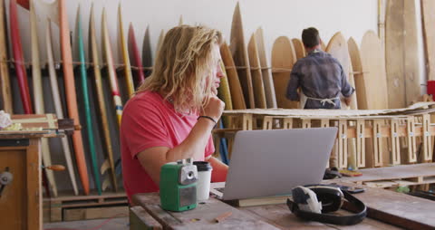 Surfboard Makers Collaborating in Workshop Using Laptop