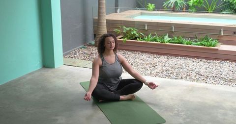 African american woman meditating on patio yoga mat near pool practicing mindfulness