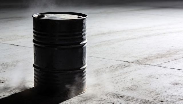 Steaming industrial steel drum with bung holes casting long shadow on concrete warehouse floor