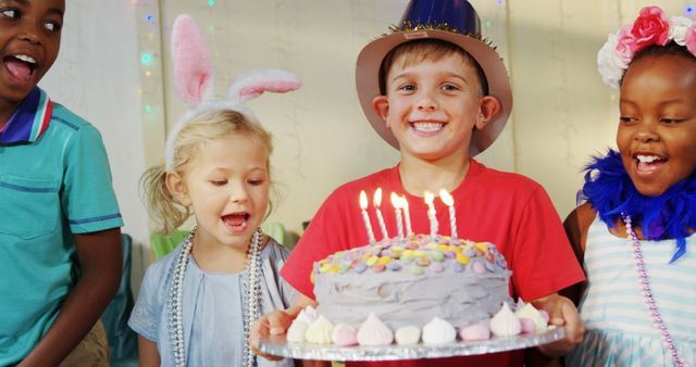 A diverse group of children celebrates a birthday party, with a young boy holding a cake with lit candles, ready to make a wish, with copy space. Joy and excitement are evident on their faces as they participate in the festive occasion.