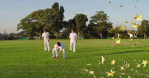 Cricket fielding team picking ball on grass with gold star overlay during sunset practice