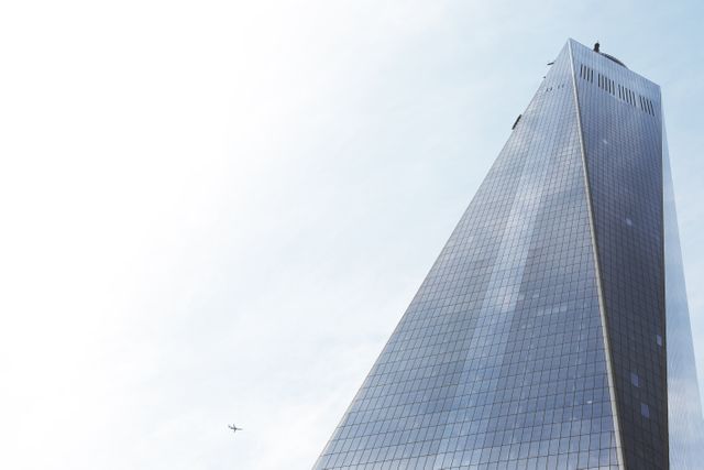 One World Trade Center, also known as Freedom Tower, rises tall against a clear blue sky with an airplane flying nearby. This image is ideal for use in travel brochures, architectural design portfolios, business promotions, or any editorial content related to urban development and iconic structures.