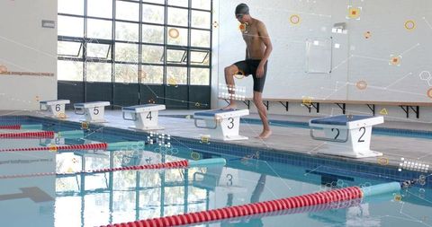 Male swimmer preparing on starting block 3 at indoor pool with reflections and geometric lines