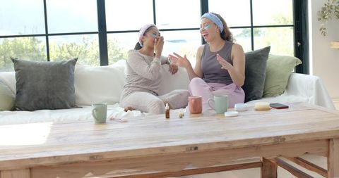 African american women sharing skincare and laughing on couch during relaxing home spa
