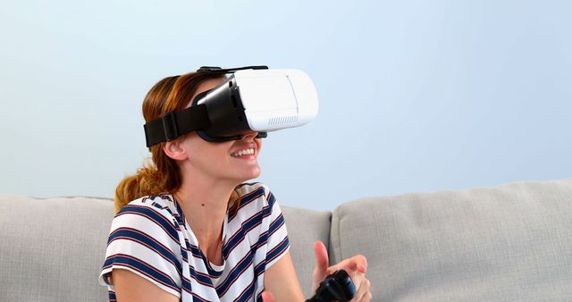 Woman wearing virtual reality headset gaming while relaxing on sofa. Great for illustrating modern lifestyle, technological advancements, and home entertainment concepts in advertisements, blogs, and technology reviews.