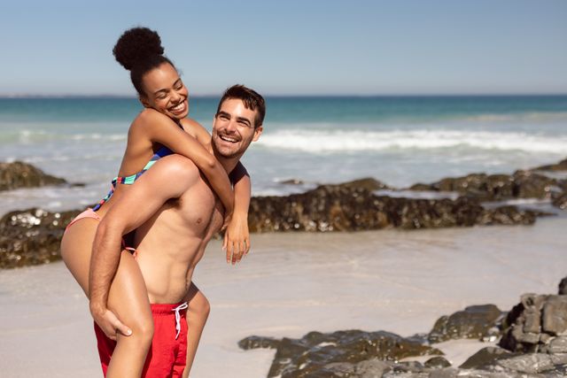 Man giving piggyback to woman on beach in the sunshine - Download Free Stock Photos Pikwizard.com