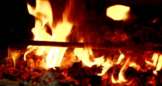 Close-up view of intense flames and glowing coals in a furnace, emitting bright fiery light. Perfect for illustrating concepts related to energy, heat, combustion, industrial processes, warmth, and barbecue or grilling backgrounds.