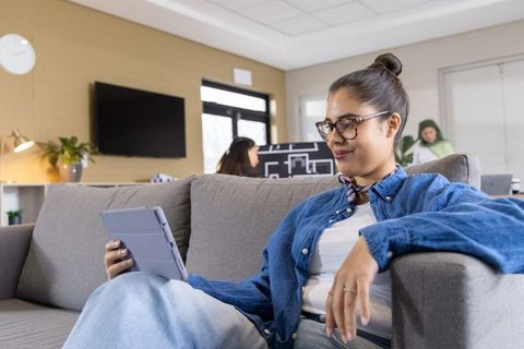 Young woman relaxing on couch using tablet in modern coworking lounge