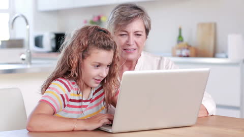 Child using laptop with grandmother in bright kitchen