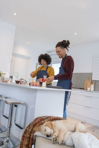 Couple preparing breakfast in modern bright kitchen with sleeping puppy