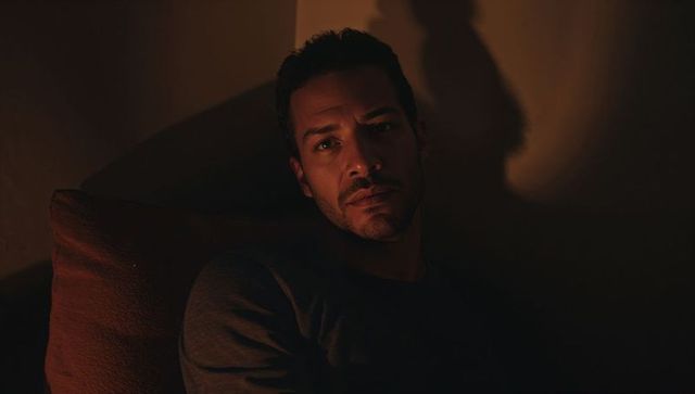 Introspective man leaning against sofa cushion in warm low-key lighting