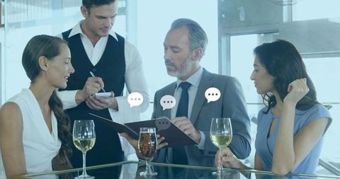 Business team discussing menu over wine, suited man reviewing notepad with speech bubbles