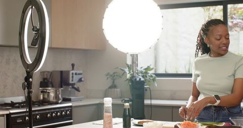 African American woman filming cooking tutorial on kitchen island with studio lighting