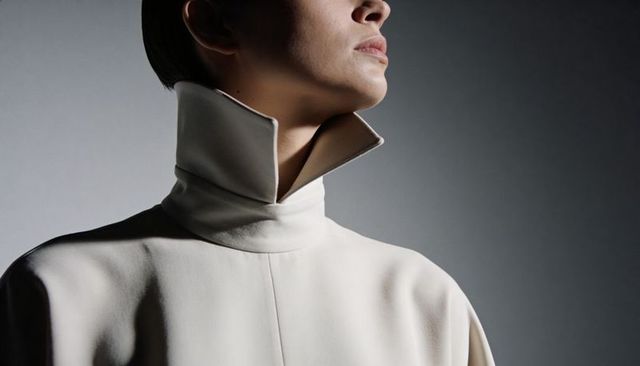 Minimalist high-collar fashion portrait portraying poised female model in cream coat