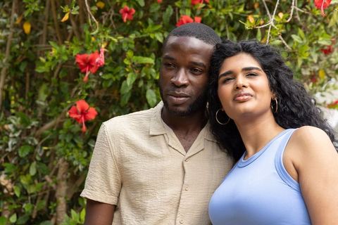 Young couple leaning together in garden with hibiscus flowers, intimate summer portrait