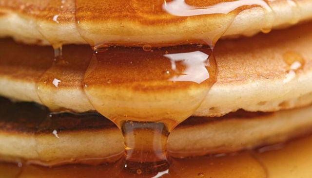 Golden maple syrup dripping over stack of fluffy pancakes close-up