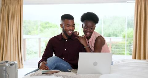 Young Couple Smiling on Bed with Laptop in Cozy Bedroom