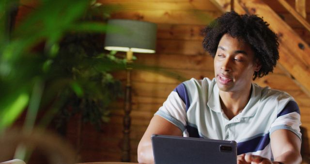 Happy african american man sitting at table and using tablet for image call, slow motion. Lifestyle, domestic life, countryside and nature concept.
