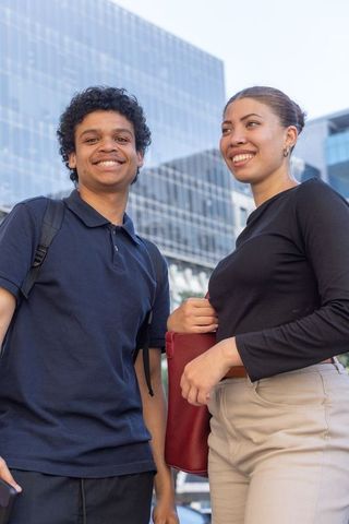 African american young friends smiling in urban plaza holding backpack and red tote