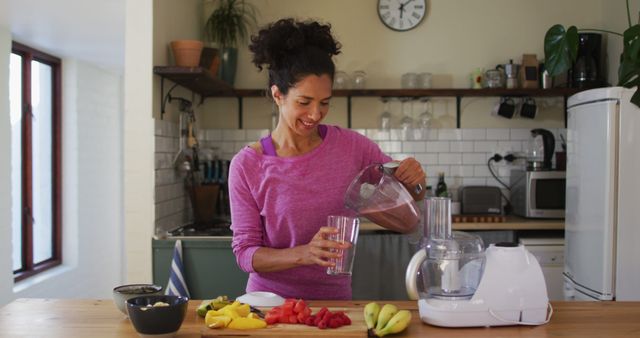 Portrait of biracial woman pouring fruit juice in a glass from juice maker in the kitchen at home. staying at home in self isolation in quarantine lockdown