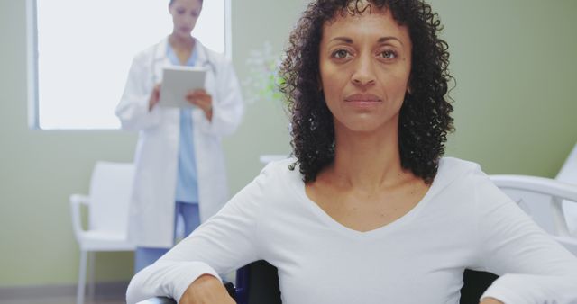 Confident Woman Sitting in Hospital with Doctor in Background - Download Free Stock Images Pikwizard.com