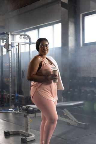 Confident african american woman finishing workout in pink activewear holding shaker