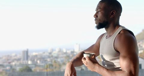 Contemplative man holding mug on balcony with urban view
