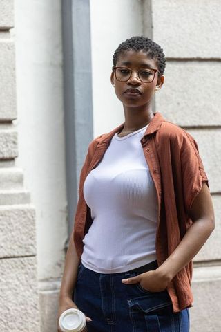 Confident woman standing and holding coffee while wearing glasses and casual urban outfit