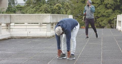 Mature African American Men Stretching and Walking on Urban Terrace with Smartphone