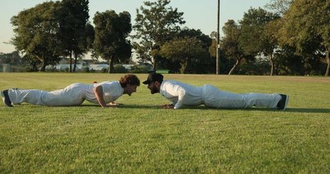 Two Male Athletes Facing Off While Planking on Grass Field Training Core Strength