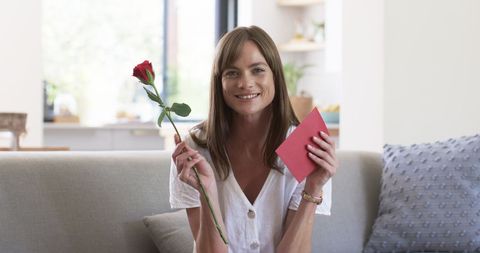 Smiling Woman with Rose and Card Celebrates Occasion at Home
