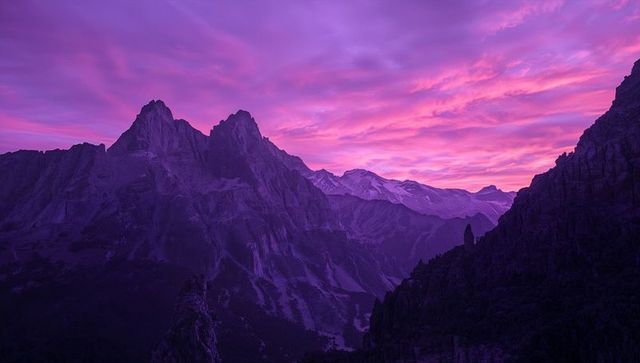 Violet sunrise over jagged alpine peaks with deep valley and dramatic ridge silhouettes