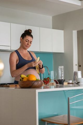 Pregnant Woman in Kitchen Preparing Fresh Fruit for Healthy Snack