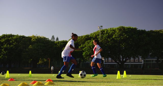 Two diverse female football players exercising with ball on sunny sports field. Active lifestyle, sport, competition, hobby and wellbeing, unaltered.