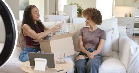 African american women unboxing package on sofa, recording casual home product review