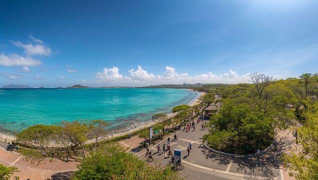 Turquoise ocean promenade with pedestrians and pedicab on sunny tropical coastal boardwalk