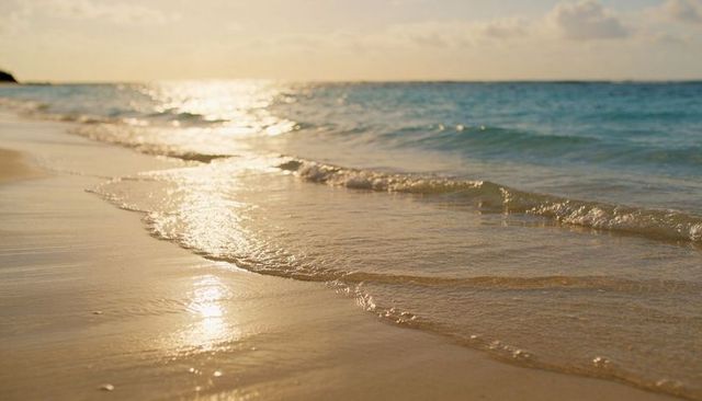 Sunlit shoreline with gentle lapping waves, wet sand reflections and serene horizon