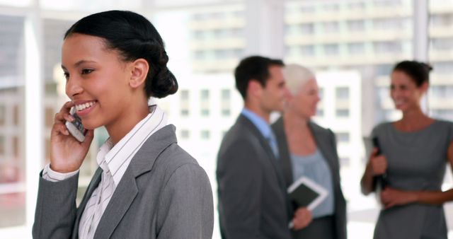 Smiling Businesswoman on Phone in Modern Office with Colleagues in Background - Download Free Stock Images Pikwizard.com