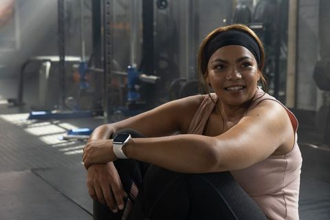 Woman Sitting on Gym Floor Smiling After Workout Wearing Smartwatch and Headband