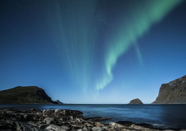 Stunning display of the northern lights sweeping over a tranquil Arctic coastline, with clear starry sky and rugged rock formations. Perfect for use in travel promotions, nature documentaries, desktop wallpapers, and inspirational posters emphasizing nature's beauty.