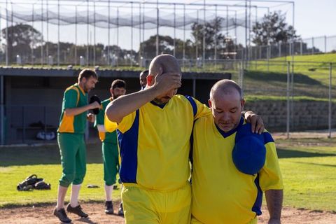 Teammates supporting injured player walking off baseball field in yellow and blue uniforms