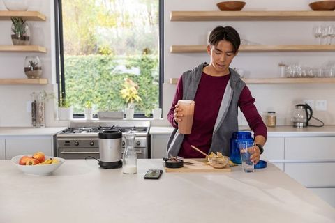 Young asian man preparing smoothie at modern minimalist kitchen island, healthy morning