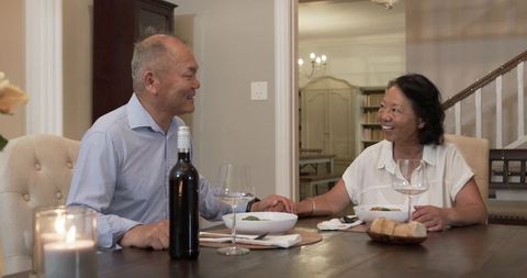 Senior asian couple holding hands over romantic dinner with wine and candlelight