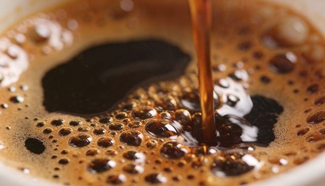Pouring dark coffee forming rich crema and glossy bubbles macro closeup surface highlights